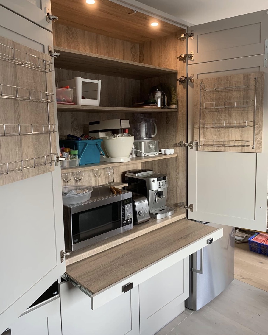A larder cupboard with its doors open, showing timber shelving, a pull-out worktop and appliances inside.