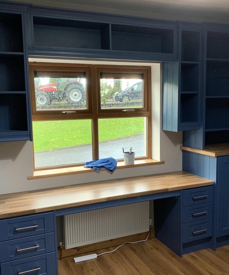 A home office painted navy blue, with timber desks, shelving and a window seat built around the window.