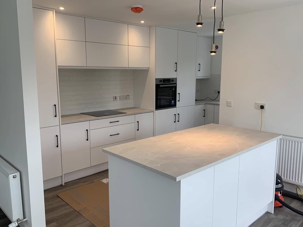 A white kitchen with black bar handles, an island and pendant lights over it.
