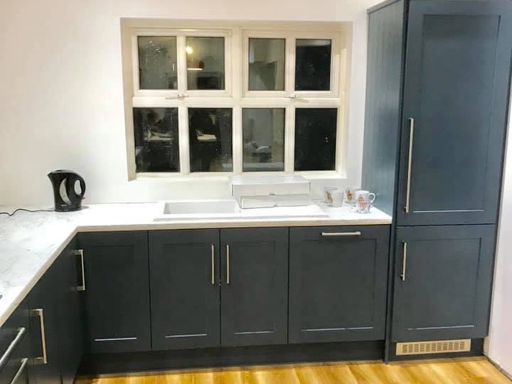 A navy blue shaker kitchen with a pale worktop and a window over the sink.