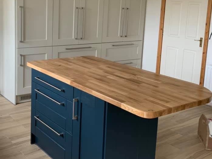 A navy painted island with a solid timber top, in front of a run of cream tall units.